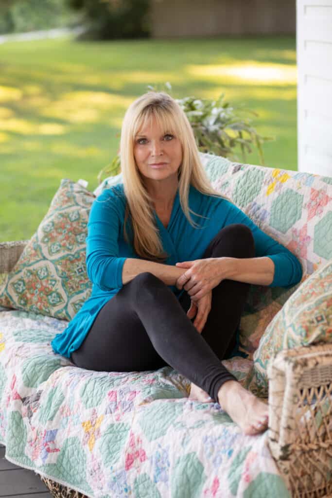 blonde woman sitting with legs up on a porch sofa on a quilt
